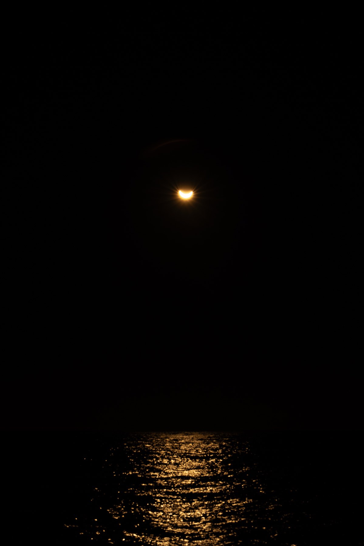 Eclipsed crescent sun low over the Atlantic with its golden reflection on the sea, seen from a boat off Cascais