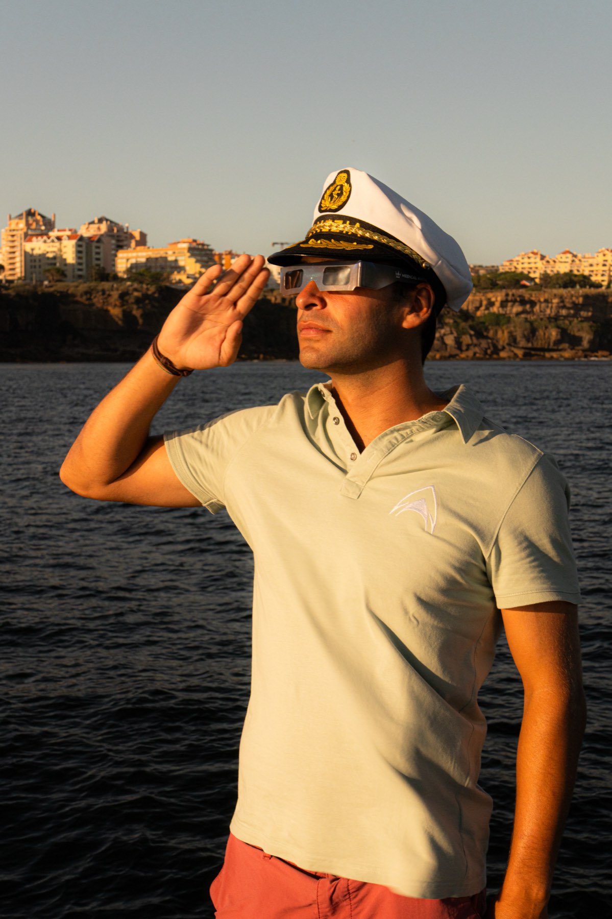 Skipper in captain's hat wearing eclipse glasses aboard a boat off the Cascais coast during the August 2026 solar eclipse