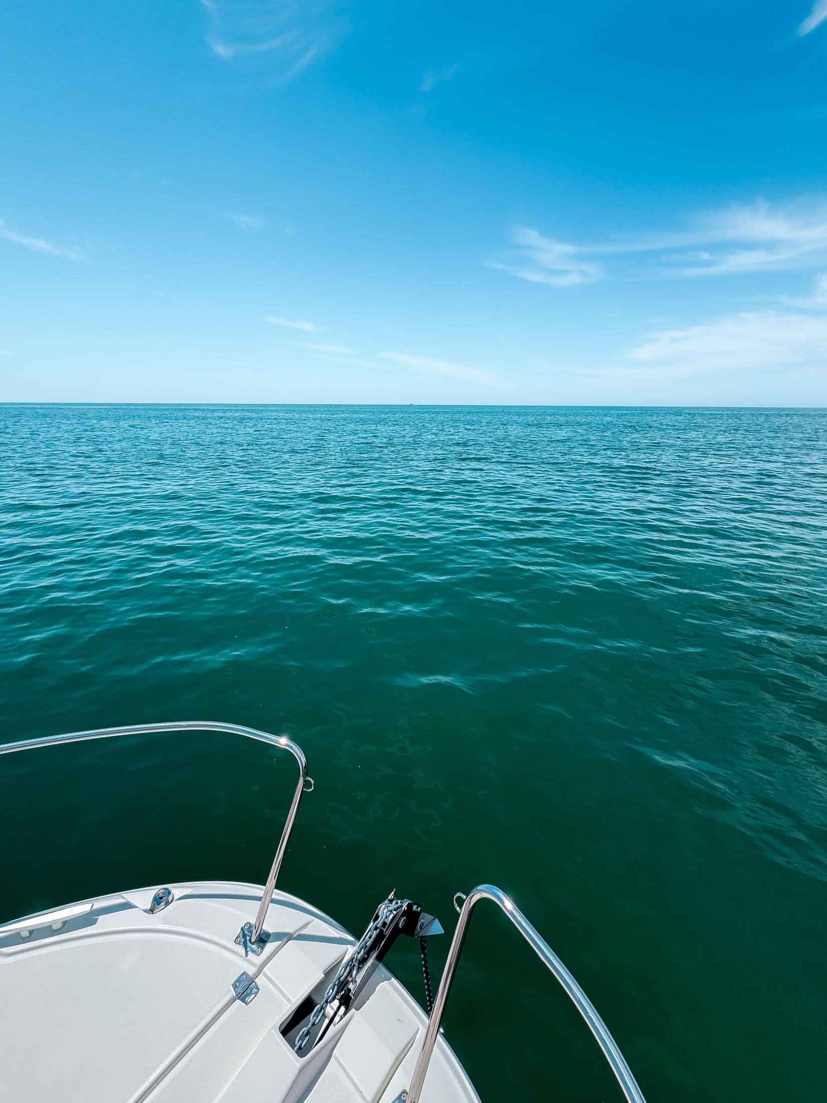 Calm turquoise water at anchor at a swimming spot near Cascais, seen from the bow of a private boat