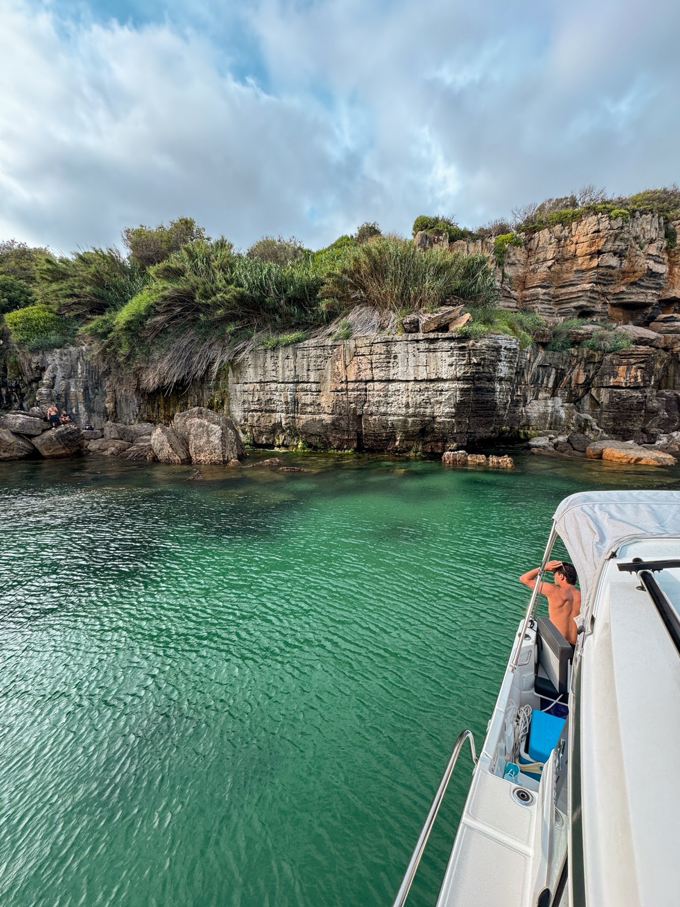 Emerald green cove below the cliffs of Cascais in the golden evening light, seen from a private boat