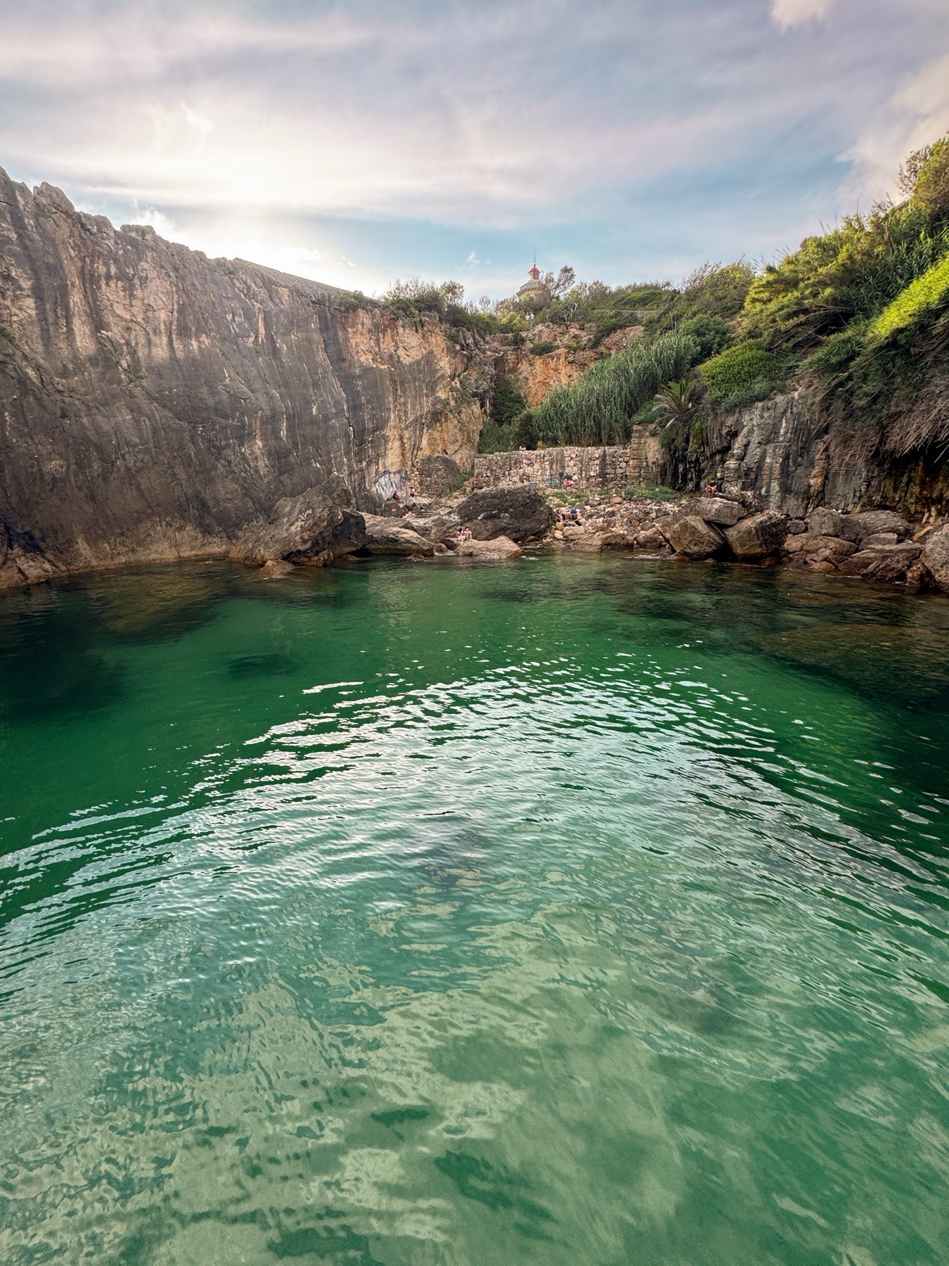 Quiet cove near Cascais at sunset with a lighthouse on the clifftop above the green water