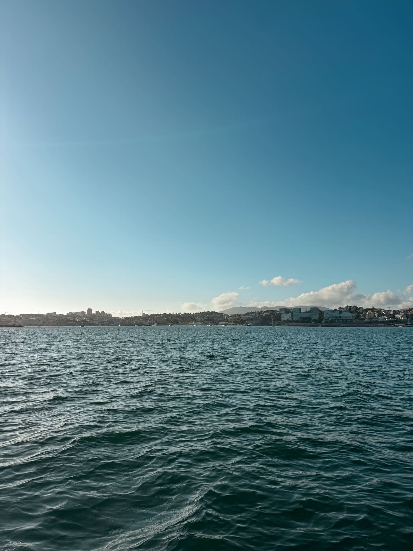 The Costa do Estoril coastline seen from a private boat off Cascais, town and hills beyond calm blue water