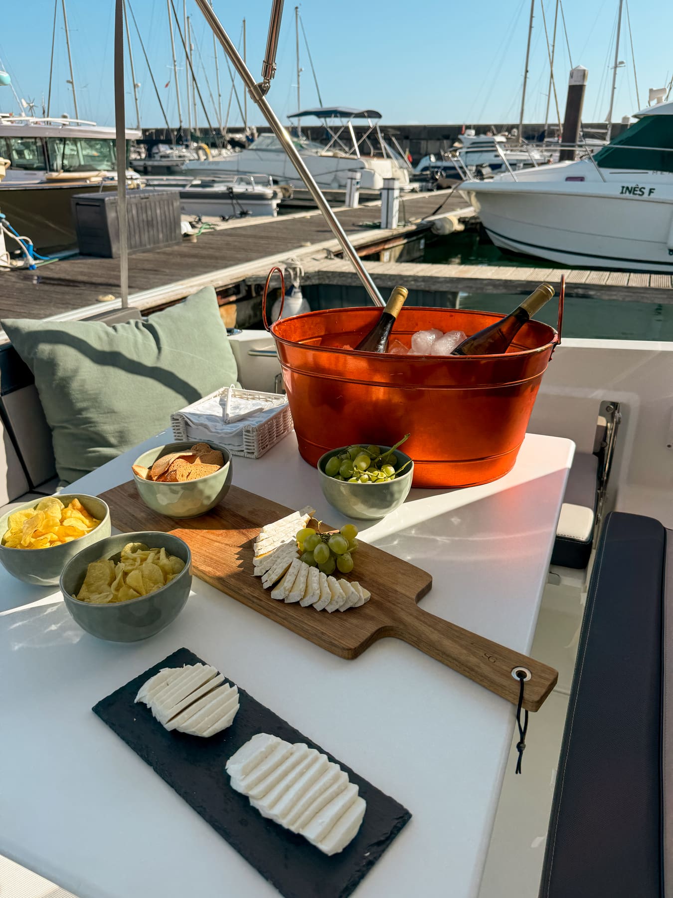 Cheese board with grapes and snacks beside chilled wine bottles on ice aboard a Nautivent boat in Marina de Cascais