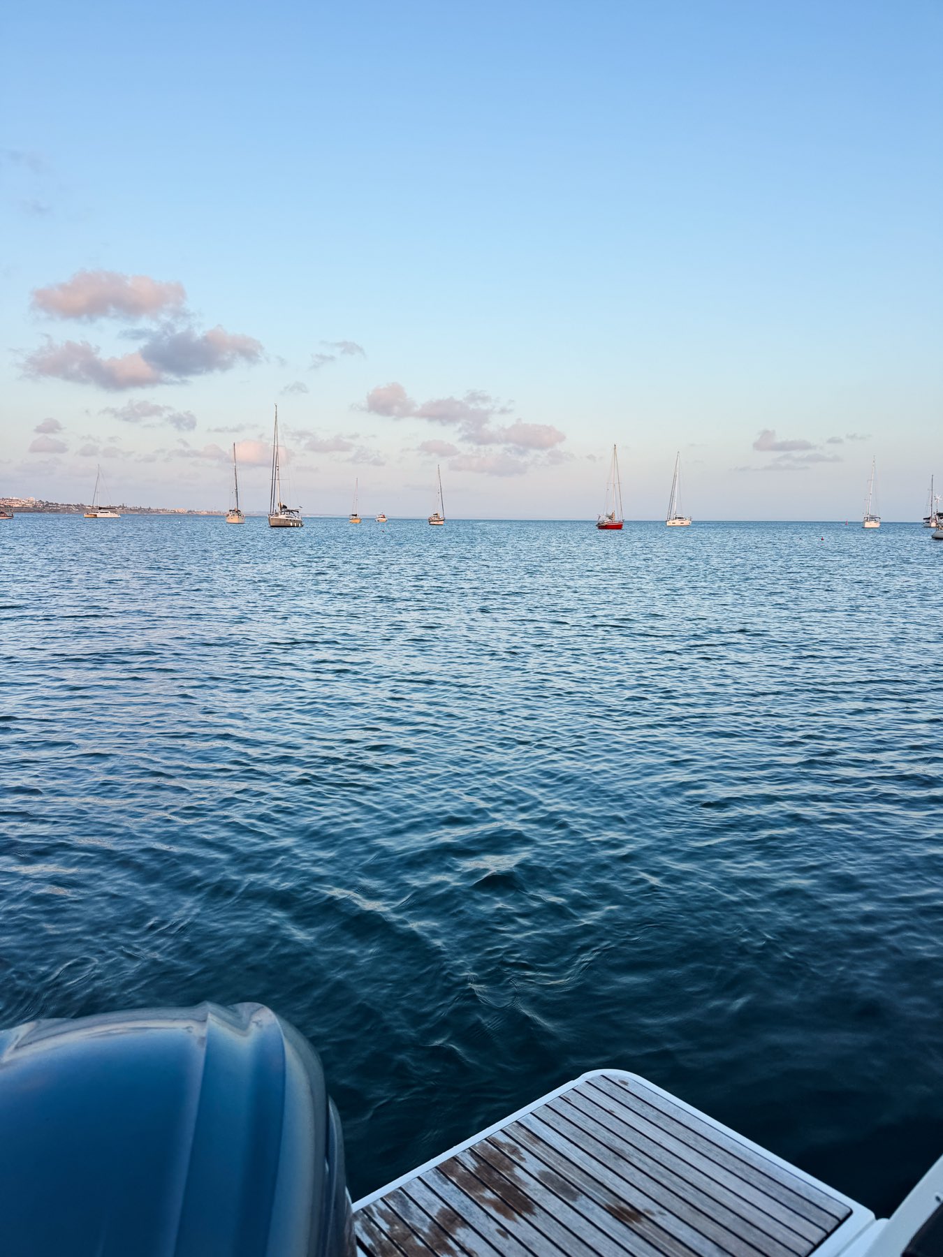 Calm evening sea in the bay of Cascais at dusk, with sailboats at anchor under a soft pink sky