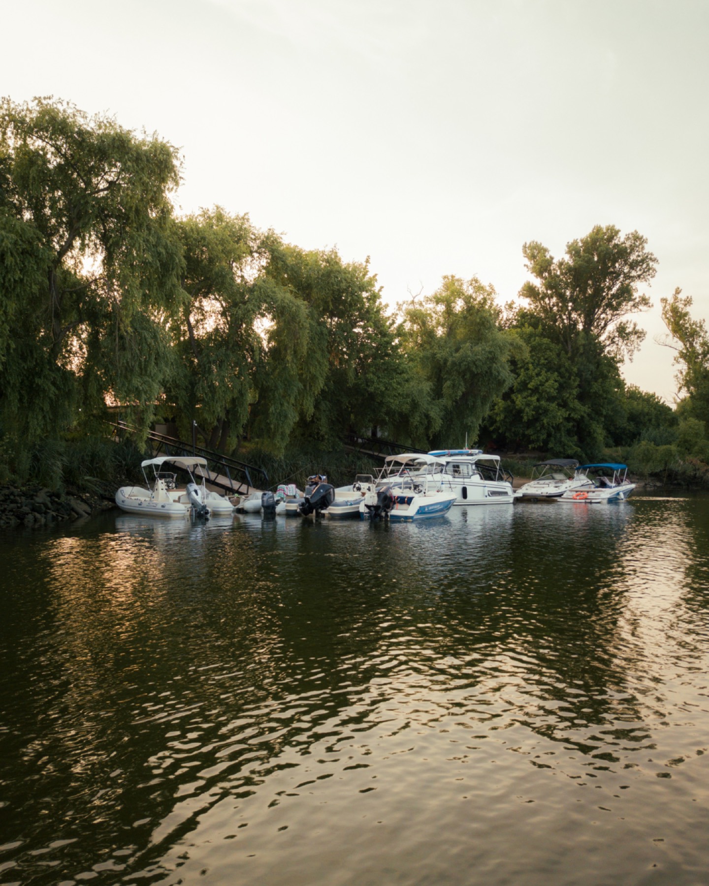 Boats moored at a quiet riverside dock in Valada at dusk, under the trees